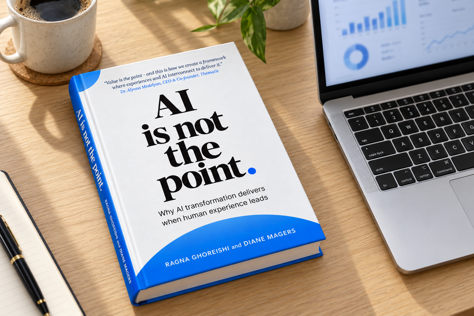 The book on a desk beside a coffee and a laptop showing dashboards